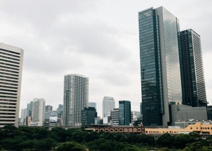 Modern skyscrapers rise above green trees under cloudy sky.